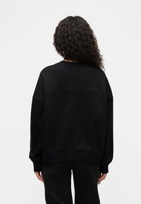 Μαύρο φαρδύ φούτερ με στρογγυλή λαιμόκοψη και χαμηλωμένους ώμους. Λεία υφή με απλό, αρθρωτό σχέδιο χωρίς εμφανείς διακοσμήσεις.