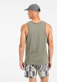 Olijfgroene tanktop van katoen met een ontspannen pasvorm, gecombineerd met gezwommen shorts met patronen in neutrale tinten en uiteenlopende vormen.