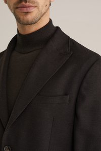 Gros plan d'un homme portant un blazer noir texturé sur un pull à col roulé côtelé noir, ne montrant que les lèvres et la ligne de la mâchoire.