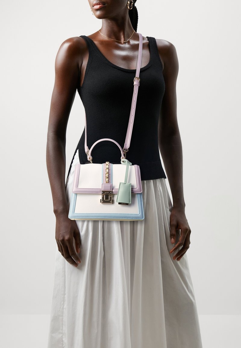 Femme portant un haut noir sans manches et une jupe blanche, avec un sac à main structuré aux couleurs pastel, bandoulière en chaîne dorée.