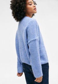 Hellblauer, flauschiger Pullover mit gerippten Bündchen und Saum, ausgestattet mit einer lockeren Passform und tiefen Schulternähten. Trägt dazu dunkelblaue Jeans.