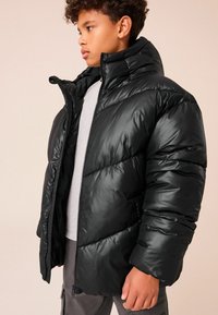Doudoune noire avec col montant, fermeture éclair et motif matelassé horizontal. Fabriquée en matériau brillant et lisse, avec une silhouette ajustée.