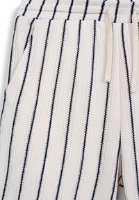 Pantaloni bianchi a maglia con strisce verticali blu navy, vita elastica e tasche laterali. Tessuto con texture e design casual.