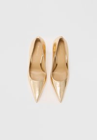 Une paire de chaussures à talons aiguilles dorées brillantes, à bouts pointus et finition texturée, vues de dessus sur un fond blanc uni.