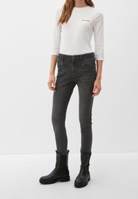 Jean skinny noirs avec une finition mate, associés à un haut fitted à manches longues blanc avec du texte noir, et des bottines noires.