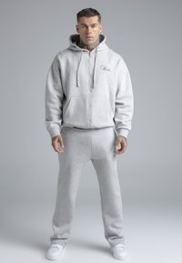 Grijze capuchontrui met voorrits en kangoeroezak, gecombineerd met bijpassende joggingbroek. Beide items hebben een logodetail.