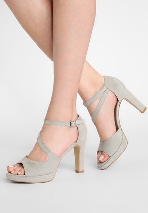 Šedé semišové sandály na vysokém podpatku s otevřenou špičkou, páskem kolem kotníku a robustním podpatkem. Mají platformovou podrážku a design překřížených pásků.