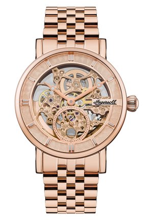 Montre mécanique en or rose avec un cadran ajouré révélant des engrenages et des bijoux complexes, dotée d'un bracelet en métal à maillons et d'une lunette texturée.