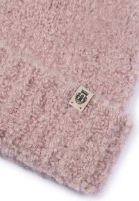 Soft, curly textured pink knitted fabric with a small beige tag featuring a black crest emblem sewn near the edge.