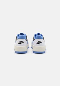 Tenisky Nike s bílým koženým svrškem s černými a světle modrými akcenty, texturovaným jazykem a modrou gumovou podrážkou.