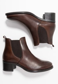 Botas de tobillo de cuero marrón con paneles laterales elásticos, punta redondeada y tacón grueso. Cuenta con un lazo en la parte trasera para ponerlas y quitarlas fácilmente.