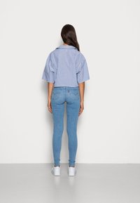 Camisa cortada a rayas azules y blancas con mangas anchas, combinada con jeans skinny de un azul claro. Zapatillas blancas completan el conjunto.