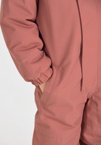 Roze waterdichte overall met elastische manchetten, zijzakken en "PRO10000" geborduurd op de mouw. Glad materiaal, praktische vormgeving.