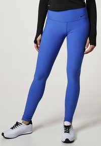 Modré strečové legíny vyrobené z hladkého, lehkého materiálu s vysokým pasem. V kombinaci s černým dlouhým rukávem a bílými sportovními botami.