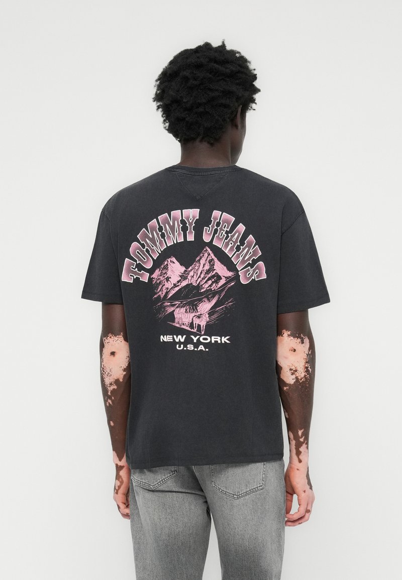 Sort bomulds t-shirt med et grafisk design af bjerge og teksten "TOMMY JEANS" i pink. Inkluderer korte ærmer og en avslappet pasform.
