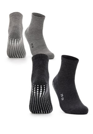 Person trägt hochgekrempelte blaue Jeans und graue rutschfeste Socken, steht mit einem Fuß flach und dem anderen auf den Zehen.