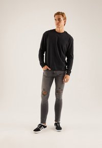 Črna majica z dolgimi rokavi, oprijete sive kavbojke z raztrganinami na kolenih in črni športni copati z belimi podplati. Preprosta, priložnostna obleka.