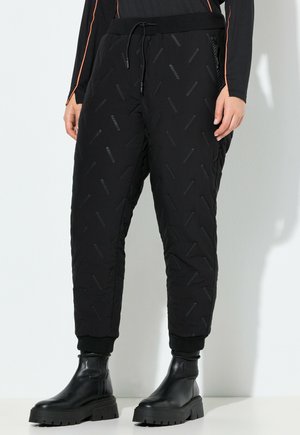 Schwarze, gesteppte Jogginghosen mit strukturiertem, erhabenen Muster, ausgestattet mit einem elastischen Bund und Bündchen. Kombiniert mit schwarzen Stiefeletten.