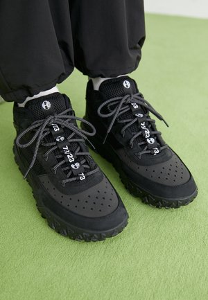 Sorte sneakers har en blanding af læder og mesh-materialer, en tekstureret gummisål, fremtrædende perforeringer og mønstrede snørebånd med numeriske accenter.