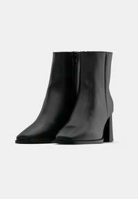 Bottes basses en cuir noir à finition lisse, avec un bout pointu et un talon épais. Équipées d'une fermeture éclair latérale pour un enfilage facile.