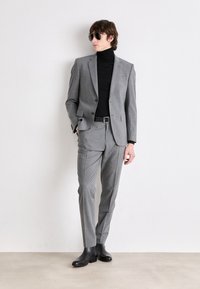 Completo grigio slim fit, tessuto texturizzato, chiusura con un bottone, abbinato a un dolcevita nero e stivaletti neri alla caviglia.
