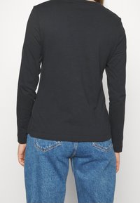 Zwarte lange mouwen top met een ronde halslijn, gemaakt van zachte stof, gecombineerd met blauwe high-waisted jeans met klassieke zakken en stiksels.