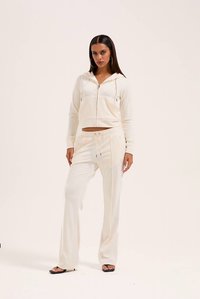 Σετ άνετης ρουχισμού σε κρεμ απόχρωση που περιλαμβάνει φούτερ με φερμουάρ και τσέπη καγκουρό, καθώς και παντελόνι με κορδόνι, και τα δύο από μαλακό, υφασμάτινο ύφασμα με υφή.