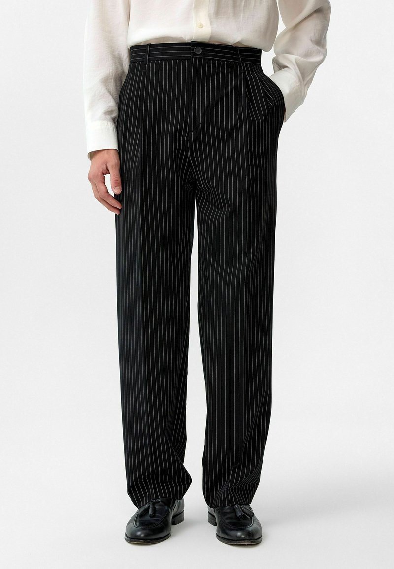 Zwarte pinstripe broek gemaakt van een gladde stof, met een rechte snit, zijzakken en een knoopsluiting in de taille.