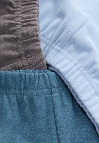 Nahaufnahme von drei gefalteten elastischen Bündchen aus braunem, hellblauem und türkisfarbenem Cordstoff.