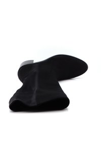 Bota de ante negro hasta la rodilla con tacón bajo y cuadrado, vista desde la abertura hacia la suela, sobre una superficie blanca.