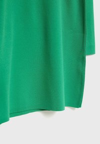 Tissu vert avec une texture à maille fine, présentant un ourlet droit et une fente latérale, sur un fond clair uni.