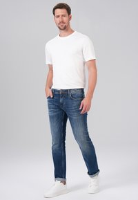 T-shirt blanche à col rond, jean en denim bleu légèrement décoloré, et baskets blanches. Look décontracté avec un design classique à cinq poches.