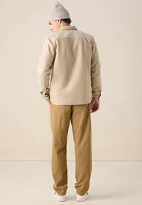 Veste en polaire beige avec un col et des accents d'épaule, assortie à un pantalon en velours côtelé doré. Le modèle porte un bonnet en tricot gris clair.