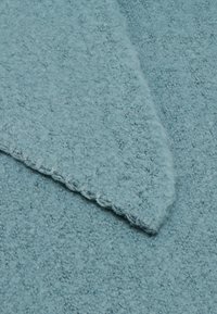 Tessuto azzurro chiaro con una superficie pelosa. Il bordo presenta una cucitura con un design a onde.