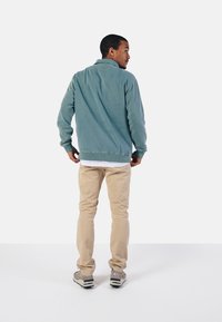 Sudadera de textura suave en azul claro, con cuello, puños y dobladillo acanalados. Combinada con pantalones beige claros y zapatillas grises.