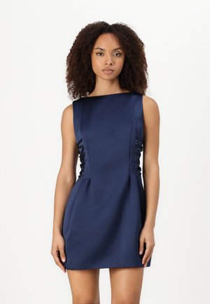 Robe sans manches bleu marine avec un décolleté carré, des découpes sur les côtés et des détails à lacets. Matériau lisse avec une silhouette ajustée.
