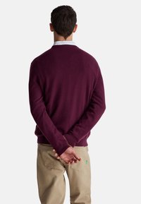 Bordowy sweter wykonany z miękkiego dzianinowego materiału, z okrągłym dekoltem i ściągaczami przy mankietach, połączony z khaki spodniami z tylnymi kieszeniami i zieloną metką z logo.