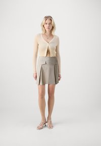 Lys beige ribbestrikket cardigan med v-hals og knapplukking, sammen med et lysegråt plissert skjørt med to frontlommer og kant over kneet.