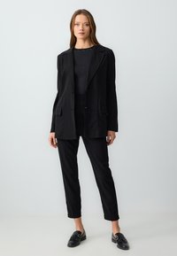 Blazer nero su misura con rever a punta, abbinato a pantaloni slim fit dello stesso colore. Top nero con delicati dettagli simili a gemme. Mocassini neri.