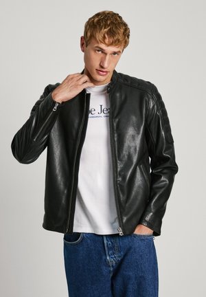 Schwarze Lederjacke mit Reißverschluss, gerippte Schultereinsätze und taillierte Passform, getragen über einem weißen T-Shirt und blauen Jeans.