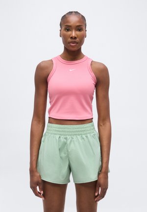 Femme athlétique de face portant un crop top rose sans manches et un short de sport vert clair à taille élastique sur un fond uni.