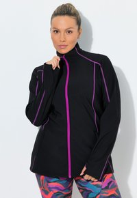 Sort atletisk jakke med lilla lynlåse og syninger, med høj krave og lange ærmer, kombineret med farverige mønstrede leggings.