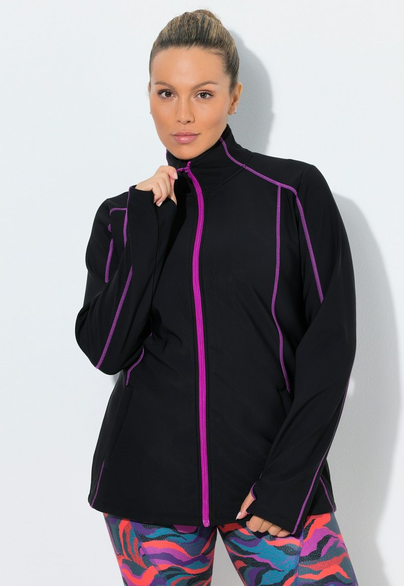 Sort atletisk jakke med lilla lynlåse og syninger, med høj krave og lange ærmer, kombineret med farverige mønstrede leggings.