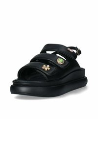 Black leather sandals with three wide straps, embellished with gold-tone accents and a green stone, featuring a thick platform sole.