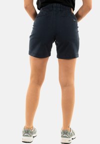 Pantalones cortos de algodón azul marino con un ajuste cómodo. Cuenta con una cinturilla, bolsillos traseros y dobladillo terminado. Combinados con zapatillas deportivas grises.