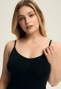 Schwarzes Camisole mit dünnen Trägern, das ein strukturiertes, gerafftes Design an der Brust und einen glatten, körperbetonten Schnitt aufweist.