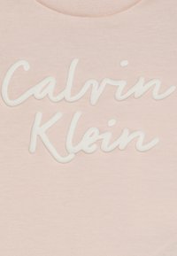Világos rózsaszín pamut póló, amelyen emelt fehér hímzett felirat szerepel: "Calvin Klein." Simító textúrájú és klasszikus kerek nyakú dizájnnal rendelkezik.
