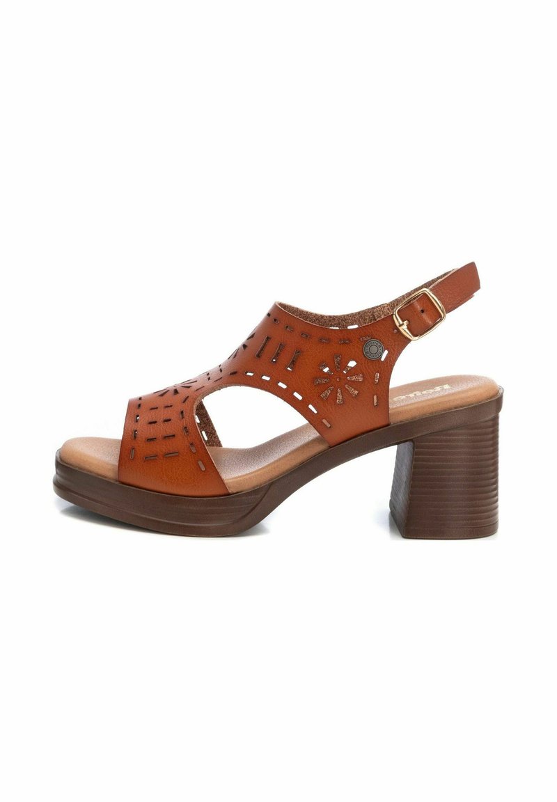 Sandalias de cuero marrón con diseños recortados, correa ajustable en el tobillo y un tacón grueso marrón. Plantilla acolchada para mayor comodidad.