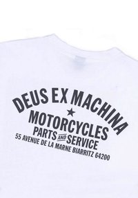 White T-shirt featuring bold black text reading "DEUS EX MACHINA MOTORCYCLES PARTS and SERVICE" with a star and address details below.
