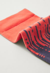 Textil med en strukturerad väv i livlig korallfärg med kontrasterande marinblå mönster, som visar en vågig design längs ena kanten.